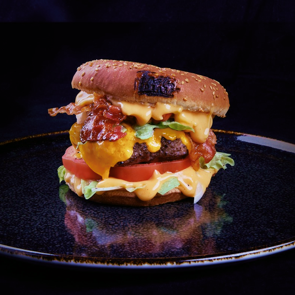 Burger mit Beef Burger Patty, geschmolzenem Cheddar, krossem Bacon, Eisbergsalat, Tomatenscheiben, roten Zwiebelringen und White Smoked BBQ Dip.